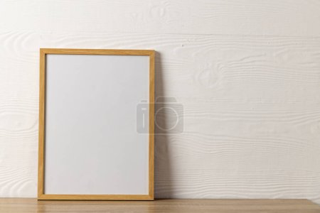Foto de Marco de madera vacío con espacio de copia en la mesa contra la pared blanca. Simular plantilla de marco, diseño de interiores y decoración. - Imagen libre de derechos
