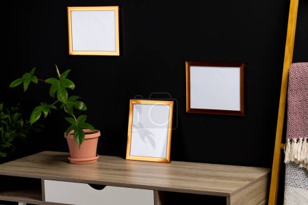 Photo for Brown empty frames with copy space and plants in pots on desk against black wall. Mock up frame template, interior design and decoration. - Royalty Free Image