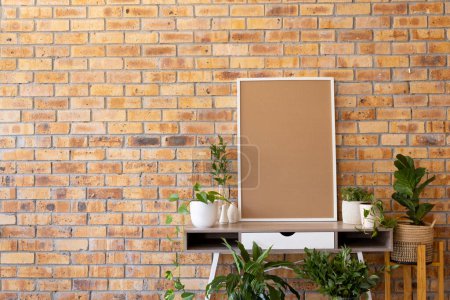 Photo for White empty frame with copy space and plants in pots on desk against brick wall. Mock up frame template, interior design and decoration. - Royalty Free Image