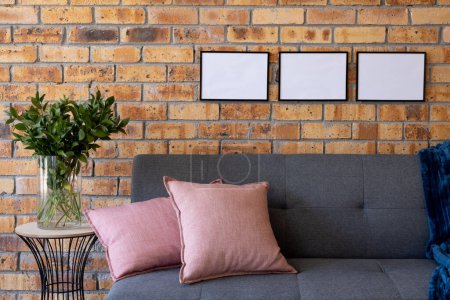 Photo for Black empty frames with copy space and plant against brick wall in room with couch. Mock up frame template, interior design and decoration. - Royalty Free Image