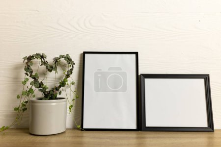 Photo for Black empty frames with copy space and heart shape plant on table against white wall. Mock up frame template, interior design and decoration. - Royalty Free Image