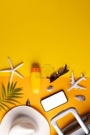 Téléchargez les photos : Smartphone avec espace de copie, modèle d'avion, valise, crème solaire, chapeau de paille sur fond jaune. Voyages, transports et vacances. - en image libre de droit