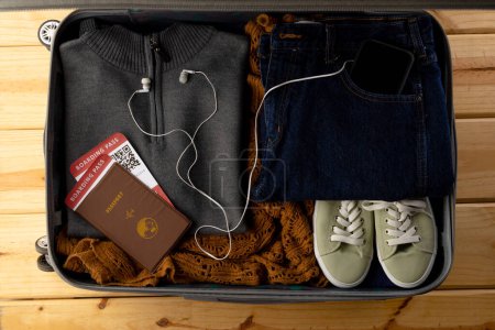 Photo for Suitcase with clothes, shoes, passport, tickets, smartphone and earphones on wooden background. Travel and vacation. - Royalty Free Image