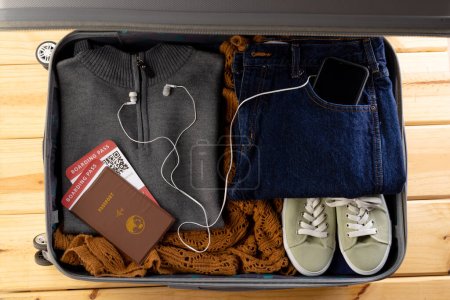 Photo for Suitcase with clothes, shoes, passport, tickets, smartphone and earphones on wooden background. Travel and vacation. - Royalty Free Image