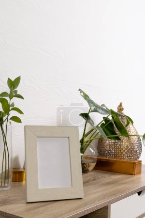 Téléchargez les photos : Vertical de cadre en bois vide avec espace de copie sur l'étagère et les plantes dans des pots contre le mur blanc. Modèle de cadre maquillé, design d'intérieur et décoration. - en image libre de droit