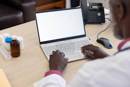 Téléchargez les photos : Médecin afro-américain utilisant un ordinateur portable avec un espace de copie à l'écran au bureau du médecin. Hôpital, médecine, santé et communication. - en image libre de droit