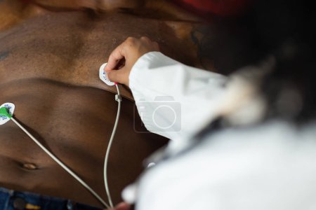 Téléchargez les photos : Partie médiane d'une femme médecin biraciale examinant un patient afro-américain, faisant un test d'ecg. Hôpital, médecine et santé. - en image libre de droit