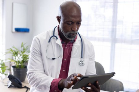 Foto de Médico afroamericano usando estetoscopio usando tableta en el consultorio del doctor. Hospital, medicina, salud y comunicación. - Imagen libre de derechos