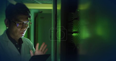 Foto de Composición de luz verde sobre hombre de negocios asiático utilizando tableta en la sala de servidores. Tecnología, informática y concepto de seguridad online imagen generada digitalmente. - Imagen libre de derechos