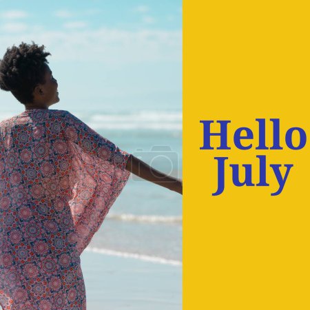 Foto de Composición de hola julio texto sobre mujer afroamericana en la playa. Verano, julio, sol, relajante y vacaciones concepto de imagen generada digitalmente. - Imagen libre de derechos