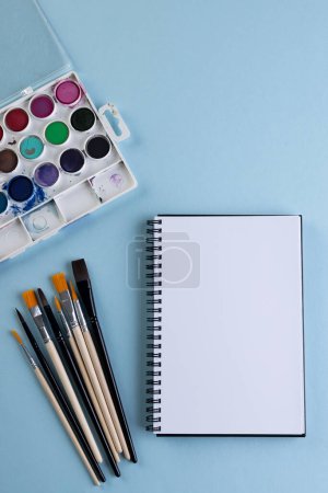 Photo for Close up of paints, notebook and brushes with copy space on blue background. Back to school, art, painting, school materials, learning, school and education concept. - Royalty Free Image