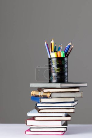 Photo for Stack of books and notebooks with pencil container on top and copy space on grey background. Reading, learning, school and education concept. - Royalty Free Image
