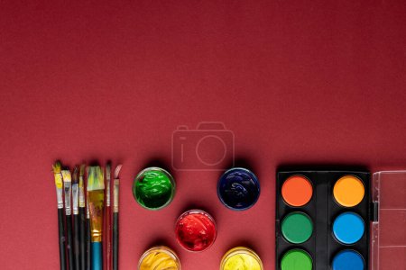 Photo for Close up of paints and brushes with copy space on red background. Back to school, art, painting, school materials, learning, school and education concept. - Royalty Free Image