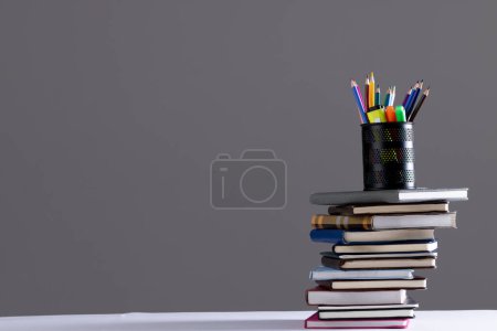 Téléchargez les photos : Empilement de livres et carnets avec récipient crayon sur le dessus et espace de copie sur fond gris. Concept de lecture, d'apprentissage, d'école et d'éducation. - en image libre de droit
