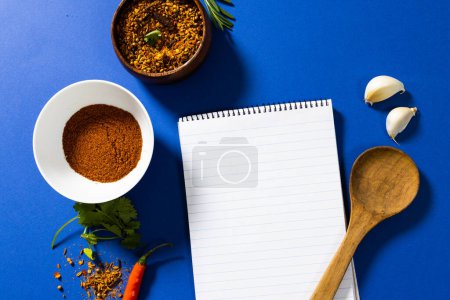 Photo for High angle view of spices and herbs with notepad against blue background, copy space. reminder, wooden spoon, food, ingredient and seasoning concept. - Royalty Free Image