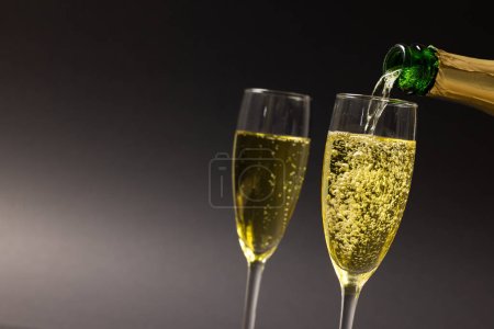 Photo for Close-up of champagne pouring in champagne flutes against black background, copy space. Drinking glass, bottle, alcohol, drink, liquor and celebration concept. - Royalty Free Image