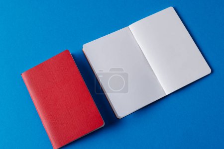 Foto de Primer plano de cuaderno rojo y libro abierto con espacio de copia sobre fondo azul. Literatura, lectura, escritura, tiempo libre y libros. - Imagen libre de derechos