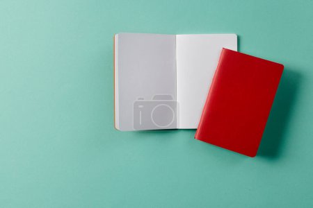 Photo for Close up of red notebook and open book with copy space on green background. Literature, reading, writing, leisure time and books. - Royalty Free Image