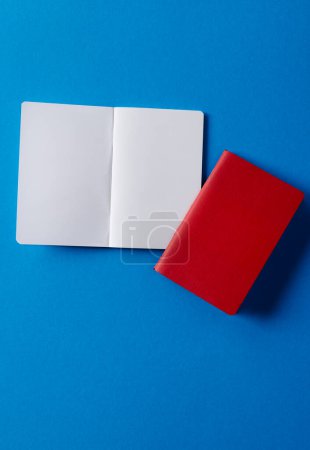 Foto de Primer plano de cuaderno rojo y libro abierto con espacio de copia sobre fondo azul. Literatura, lectura, escritura, tiempo libre y libros. - Imagen libre de derechos
