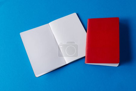 Photo for Close up of red notebook and open book with copy space on blue background. Literature, reading, writing, leisure time and books. - Royalty Free Image