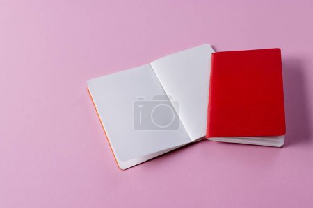 Photo for Close up of red notebook and open book with copy space on pink background. Literature, reading, writing, leisure time and books. - Royalty Free Image