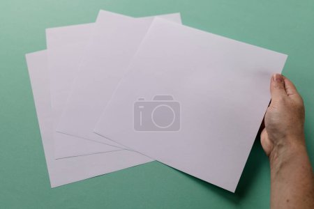 Téléchargez les photos : Main de femme caucasienne tenant un morceau de papier sur des morceaux de papier avec un espace de copie sur fond vert. Littérature, lecture, loisirs et livres. - en image libre de droit