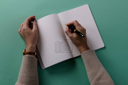 Photo for Hands of caucasian woman holding pen and writing in notebook with copy space on green background. Literature, writing, leisure time and books. - Royalty Free Image