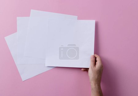 Photo for Hand of caucasian woman holding piece of paper over paper pieces with copy space on pink background. Literature, reading, leisure time and books. - Royalty Free Image