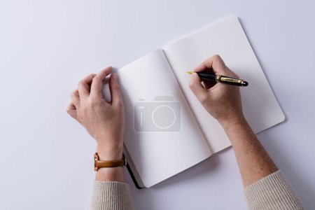 Téléchargez les photos : Mains de femme caucasienne tenant un stylo et écrivant dans un carnet avec espace de copie sur fond blanc. Littérature, écriture, loisirs et livres. - en image libre de droit