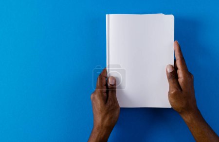 Téléchargez les photos : Mains de l'homme biracial tenant le livre avec l'espace de copie sur fond bleu. Littérature, lecture, loisirs et livres. - en image libre de droit