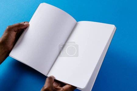 Photo for Hands of biracial man holding book with copy space on blue background. Literature, reading, leisure time and books. - Royalty Free Image