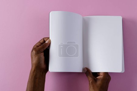 Téléchargez les photos : Mains de l'homme biracial tenant le livre avec l'espace de copie sur fond rose. Littérature, lecture, loisirs et livres. - en image libre de droit