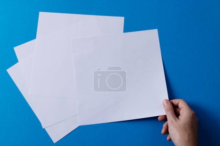 Téléchargez les photos : Main de femme caucasienne tenant un morceau de papier sur des morceaux de papier avec de l'espace de copie sur fond bleu. Littérature, lecture, loisirs et livres. - en image libre de droit