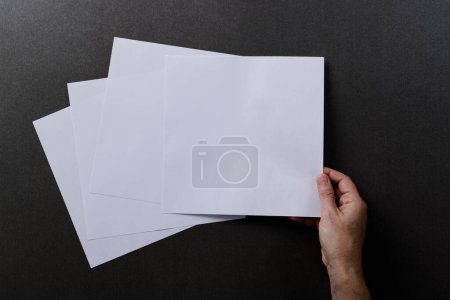 Photo for Hand of caucasian woman holding piece of paper over paper pieces with copy space on black background. Literature, reading, leisure time and books. - Royalty Free Image