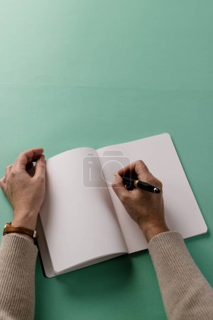 Téléchargez les photos : Mains de femme caucasienne tenant un stylo et écrivant dans un carnet avec espace de copie sur fond vert. Littérature, écriture, loisirs et livres. - en image libre de droit
