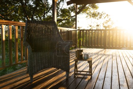 Foto de Balcón de cabaña de madera con sillón y taza de café en día soleado. Naturaleza, agricultura, verano, tranquilidad y paisaje rural. - Imagen libre de derechos