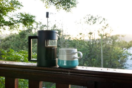 Téléchargez les photos : Gros plan de la presse à café et tasse de café frais sur le balcon par une journée ensoleillée. Nature, agriculture, été, boisson et paysage rural. - en image libre de droit