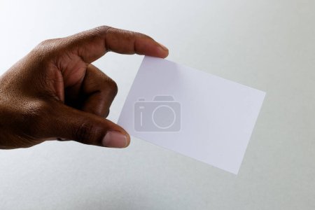 Téléchargez les photos : Main d'homme biracial tenant une carte de visite blanche avec espace de copie sur fond blanc. Concept d'espace de travail, carte de visite, papeterie et écriture. - en image libre de droit
