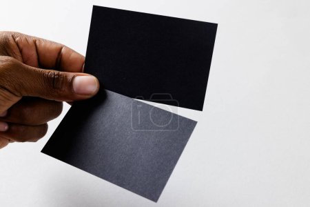 Photo for Hand of biracial man holding black business cards with copy space on white background. Business, business card, stationery and writing space concept. - Royalty Free Image