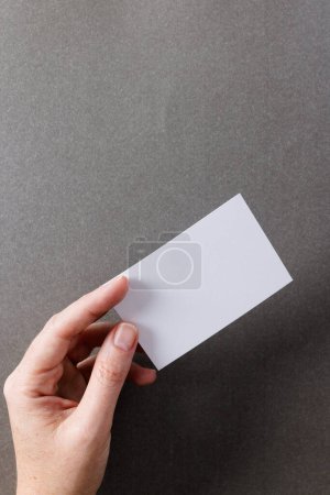 Photo for Vertical image of hand of caucasian woman with business card with copy space on grey background. Business, business card, stationery and writing space concept. - Royalty Free Image