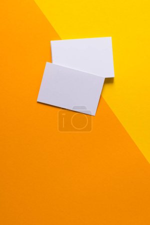 Téléchargez les photos : Image verticale de cartes de visite blanches avec espace de copie sur fond jaune et orange. Concept d'espace de travail, carte de visite, papeterie et écriture. - en image libre de droit