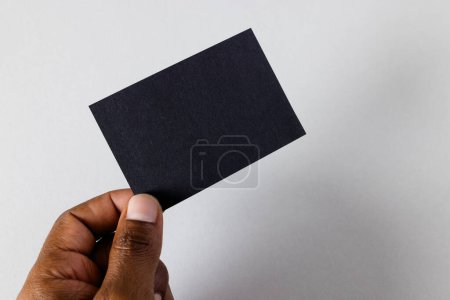 Téléchargez les photos : Main d'homme biracial tenant une carte de visite noire avec espace de copie sur fond blanc. Concept d'espace de travail, carte de visite, papeterie et écriture. - en image libre de droit