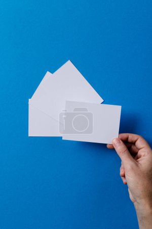 Photo for Vertical image of hand of caucasian woman with business card with copy space on blue background. Business, business card, stationery and writing space concept. - Royalty Free Image