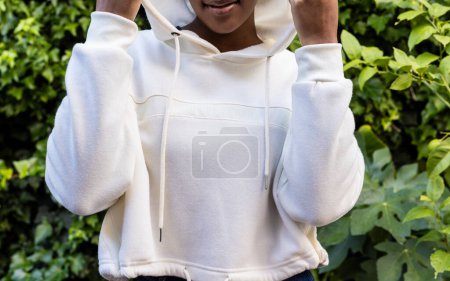 Foto de Sección media de una mujer afroamericana con sudadera blanca con capucha en el jardín. Moda, ropa casual y ropa de ocio, inalterada. - Imagen libre de derechos
