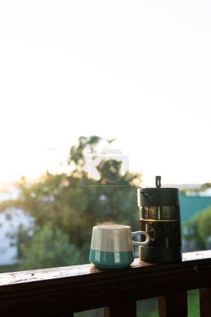 Téléchargez les photos : Image verticale de gros plan de la presse à café et tasse de café frais sur le balcon par une journée ensoleillée. Nature, agriculture, été, boisson et paysage rural. - en image libre de droit