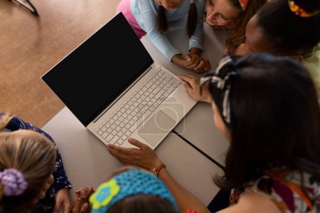Photo for High angle view of diverse female teacher and girls looking at laptop while studying online on table. Copy space, unaltered, childhood, technology, education, student, e-learning, school concept. - Royalty Free Image