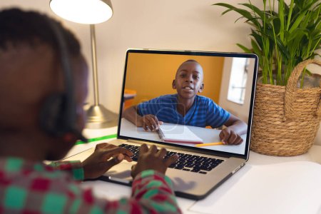 Téléchargez les photos : Africain américain garçon dans les écouteurs discuter des devoirs avec un ami lors d'un appel vidéo sur ordinateur portable à la maison. Inchangé, enfance, technologie, éducation, étudiant, en ligne, écran, e-learning. - en image libre de droit