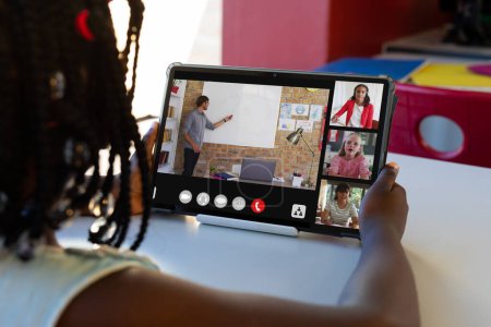 Foto de Chica afroamericana que asiste a clases en línea a través de tabletas digitales con estudiantes y profesores en pantalla. Inalterado, infancia, tecnología, educación, estudiante, e-learning y concepto casero. - Imagen libre de derechos