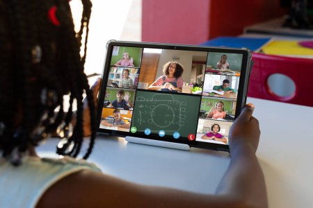 Téléchargez les photos : Afro-américaine fille tenant tablette numérique avec enseignant et étudiants à l'écran étudiant en ligne. Inchangé, apprentissage en ligne, éducation, enfance, appel vidéo, technologie et concept de la maison. - en image libre de droit