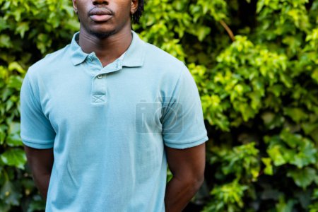 Téléchargez les photos : Milieu de l'homme afro-américain portant un polo bleu pâle dans le jardin, espace de copie. Mode, vêtements décontractés et vêtements de loisir, inchangés. - en image libre de droit